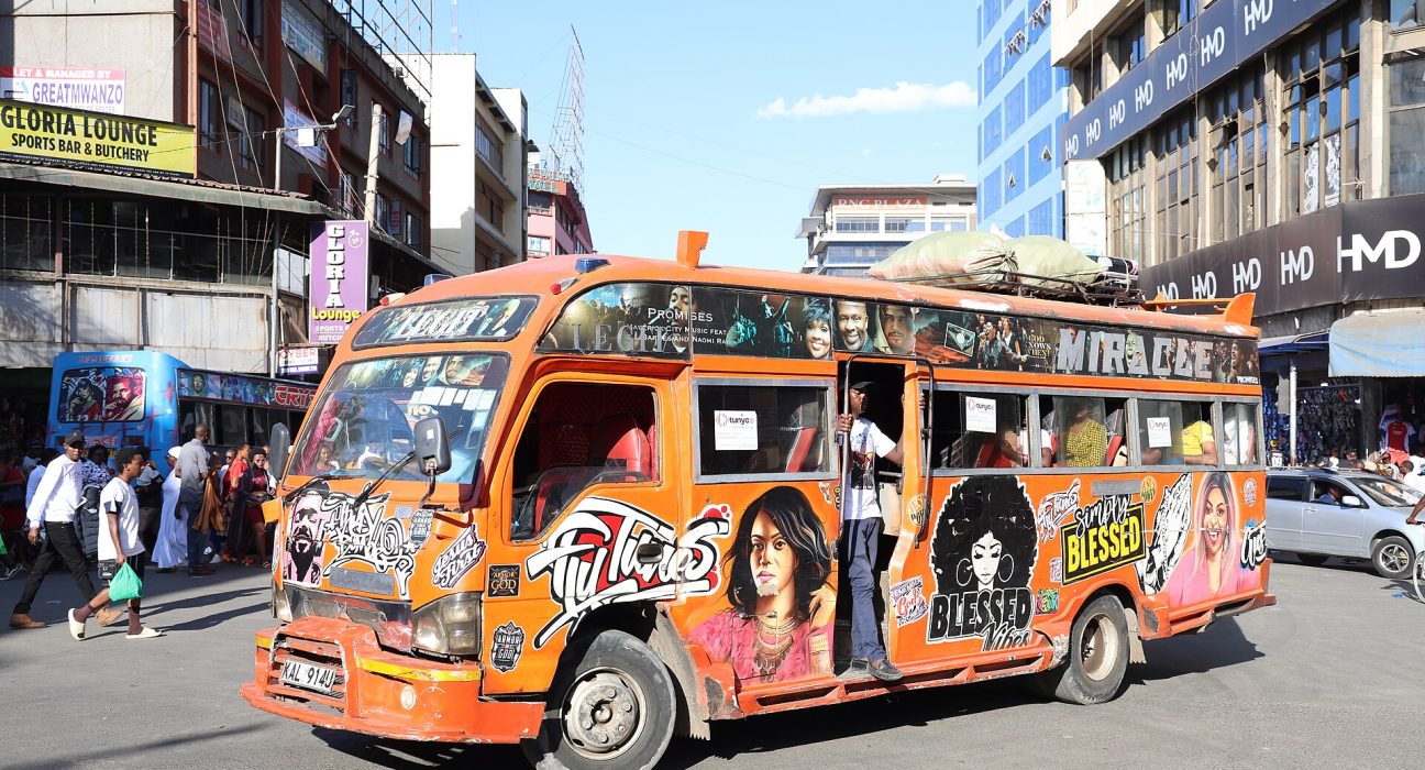 A matatu painted in bright orange artwork drives along a busy street in Nairobi