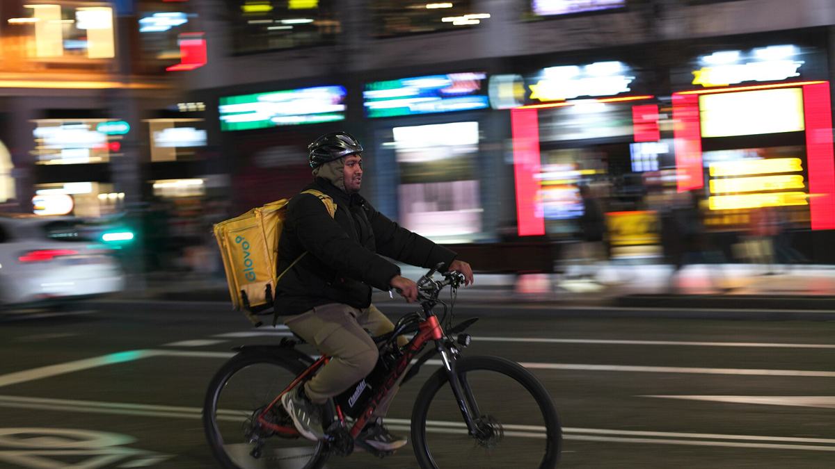 Glovo delivery rider with a yellow Glovo backpack cycling through a city street at night