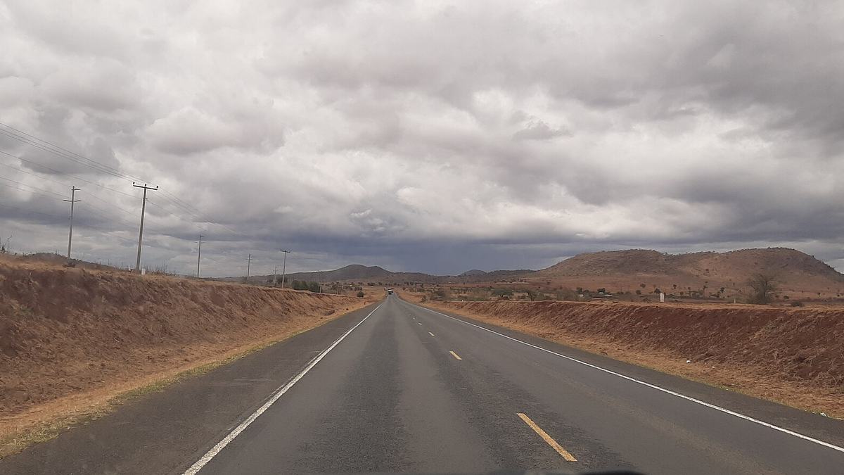 An empty stretch of the Nairobi-Mombasa highway through dry, open country under a cloudy sky