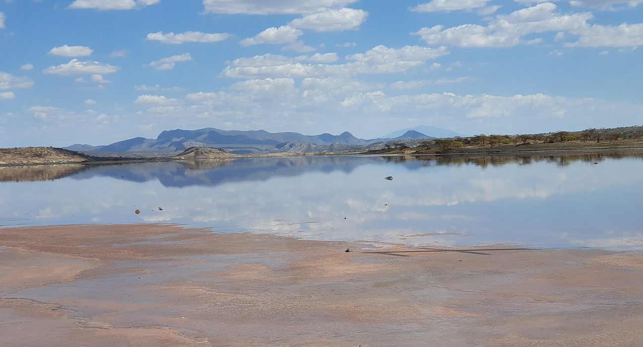 Lake Magadi in Kajiado County, with pink soda flats in the foreground and hills behind the water